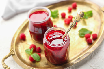 Jars with tasty raspberry jam on metal tray