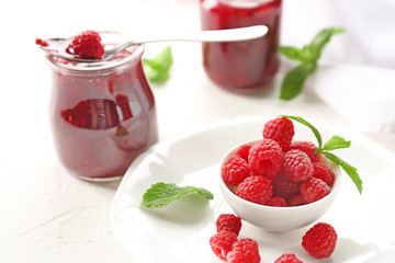 Bowl with ripe raspberries and jar of tasty jam on table