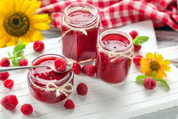 Jars with tasty raspberry jam on white board