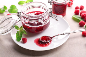 Jar with tasty raspberry jam on plate