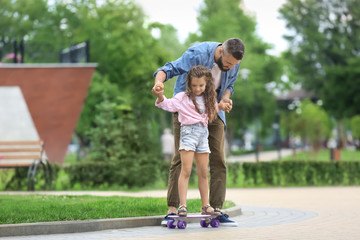 Father teaching his little daughter to ride skateboard outdoors