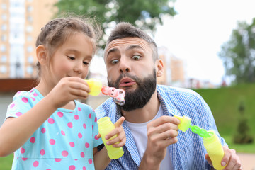 Little girl and her father blowing soap bubbles outdoors