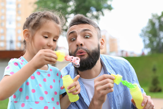Little girl and her father blowing soap bubbles outdoors - Powered by Adobe