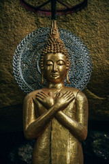 Golden Buddha statue having arms crossed on the chest with closed eyes meditating. Buddha statue with a golden hat and background is the silver plate at the back of the face. 