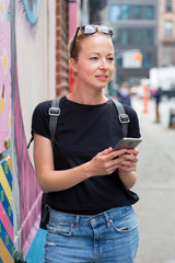 Closeup of female hipster with smart phone. Woman using smart phone app guite on city break weekend trip to East Village, New York city, USA.