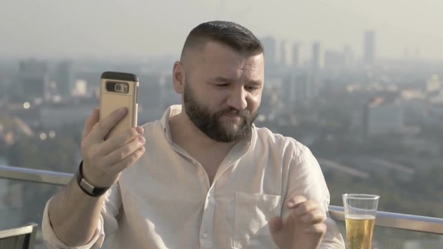 Man drinking beer in the skybar and doing selfies on smartphone
