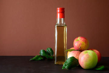 Apple vinegar in glass bottle and fresh apples on brown wooden desk