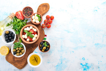Cooking a caprese salad. Mozzarella cheese, cherry tomatoes, olives, basil leaves. Top view. On a white stone table. Free space for text.
