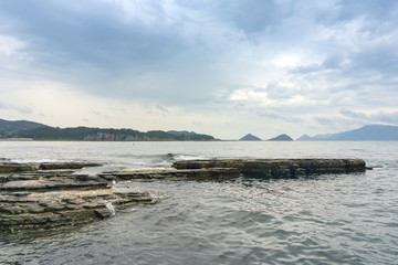 The black layers of sediment rock with shells lie slightly tilted toward the sea at Sangjogam Country Park in Geosong, South Korea