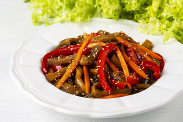 Vegetable salad. Aubergines fried, pepper, carrots on a white plate. The concept of healthy eating. White wooden background.