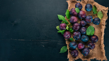 Fresh plums with leaves. Fruits. On a black wooden background. Top view. Free space for your text.