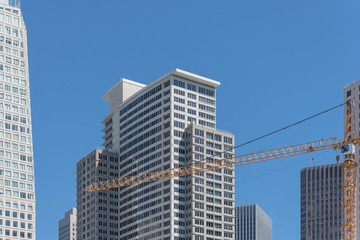 Obraz premium Working yellow crane near completed building in downtown San Francisco, California, USA. Construction and industrial background office and residential skyline, clear blue sky