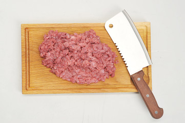 Finely chopped meat on a light wooden board. Then the knife is for cutting. White background. Close-up. View from above.