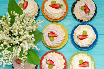 Strawberry pavlova cake nests, meringue decoration on wood table with lily of the valley flowers.