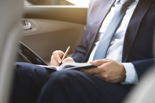 Man in a business suit write on notebook with laptop in the car