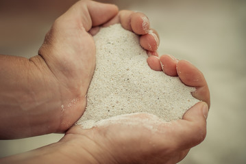 Close up hands holding white sand heart shape