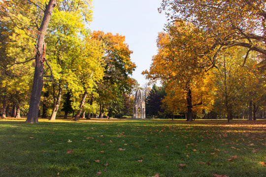 Autumn landscape city park, Gothic architectural fragment of historic tower in the middle, green grass with autumn leaves and colourful huge old trees around, The Janko Kral City Park, Bratislava