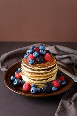 Stack of pancakes with fresh blueberry, raspberry and blackberry on brown plate