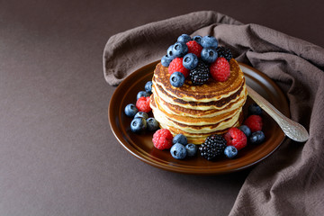Stack of pancakes with fresh blueberry, raspberry and blackberry on brown plate