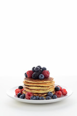 Stack of pancakes with fresh blueberry, raspberry and blackberry on white plate