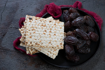 Metal tray with date fruits and matzo bread, studio shot over grey stone background, selective focus