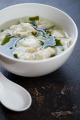 Closeup of a white bowl with chinese wonton soup, selective focus, vertical shot