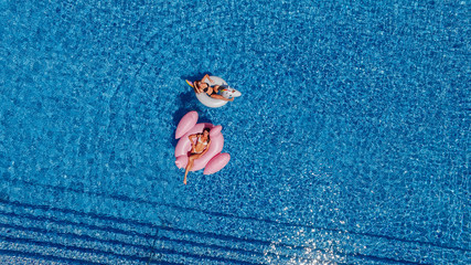 Two happy young beautiful girls with beautiful figures swim in the pool for flamingos and unicorns. Top view. © Тарас Нагирняк