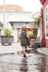  Kleinkind spielt in Wasser Pfütze. Blond child girl plays with water.