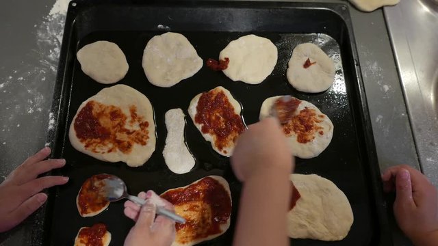Top view, on hands spread tomato sauce on small pizzas