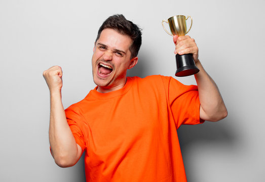 Young handsome man in orange t-shirt with golden cup. Studio image on white background