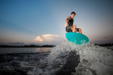 Active and strong man jumping on wakesurf down the river waves at the sunset