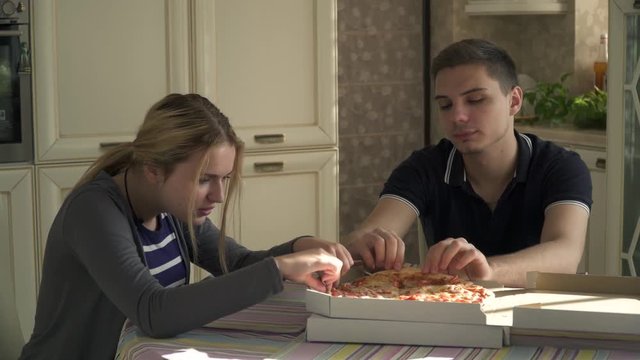 Young couple eating pizza in the kitchen