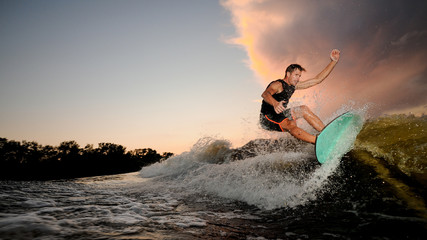 Handsome muscular young man wakesurfing down the river waves - obrazy, fototapety, plakaty