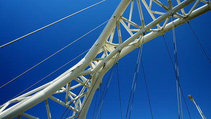 Detail of modern white metal bridge with steel support wires seen from below with blue sky © Kraft74