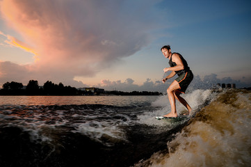 Muscular man riding on wakesurf down the river during sunset