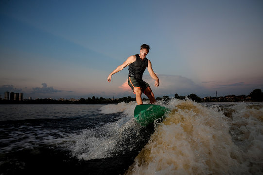 Handsome athletic man riding on wakesurf down the river during sunset