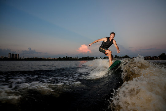 Handsome muscular man riding on wakesurf down the river during sunset