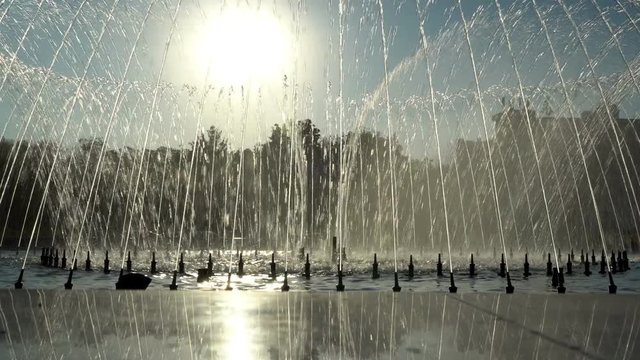 Dancing fountain in the city Park at sunset. Water jets fly into the sky in the rhythm of music against the background of the sun in the city Park. 4K, 25 fps.