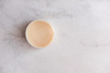 Spa cosmetics, open jar with skin care product on white marble background from above. Beauty blogging concept. Copyspace