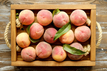 Bunch of ripe organic peaches in pile on wooden tray with rope handles on grunged wood textured table. Local produce harvest heap. Clean eating concept. Background, top view, close up, copy space