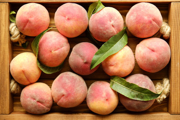 Bunch of ripe freshly picked organic peaches in pile on wooden tray of farmers market. Peach harvest heap. Healthy vegan raw snack. Clean eating concept. Cropped shot, background, top view, flat lay.