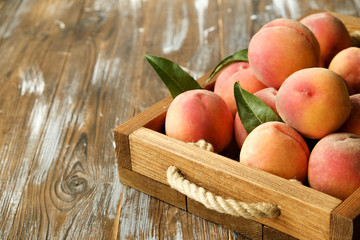 Bunch of ripe organic peaches in pile on wooden tray with rope handles on grunged wood textured table. Local produce harvest heap. Clean eating concept. Background, top view, close up, copy space