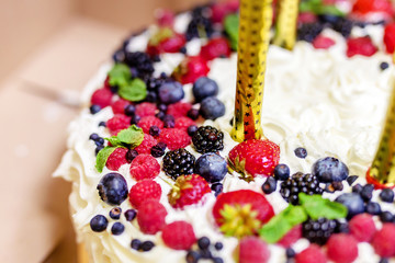 Close-up beautiful tasty big natural cake dressed with fresh berries. Fireworks candles prepared in dessert for birthday party