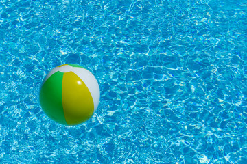 Inflatable multicolored ball floating on swimming pool water, with copy space, summer recreation concept.
