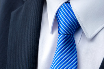 Close-up of a blue striped tie on a white shirt and a businessman suit.