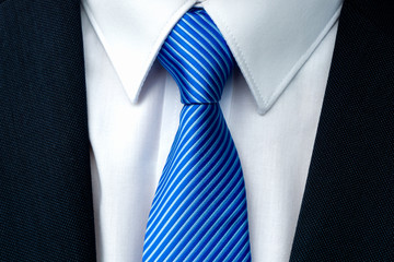 Close-up of a blue striped tie with withe shirt and dark businessman suit.