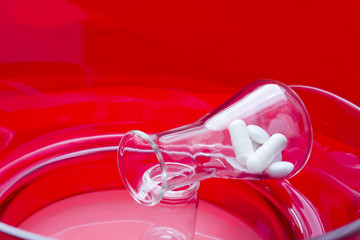 Drug design. Erlenmeyer flask with white drugs on red background