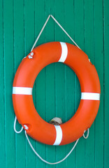 An orange life buoy on a green wooden wall