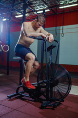 Fit young man using exercise bike at the gym. Fitness male using air bike for cardio workout at cross training gym.