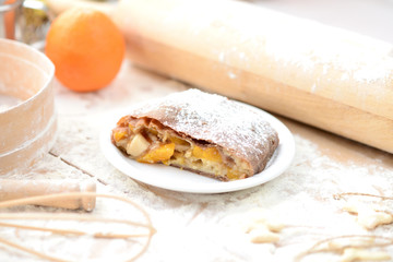 strudel (roll strudel) with orange on a wooden board with flour